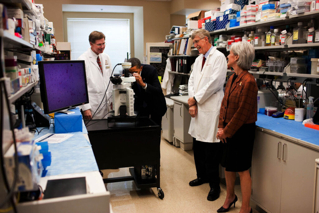 President Barack Obama looks through a microscope during a tour of an oncology laboratory at the National Institute of Health in Bethesda, Md., Sept. 30, 2009. Others present include Dr. Marston Linehan, left, Dr. Francis Collins, Director of NIH, second from right, and Health and Human Services Secretary Kathleen Sebelius. (Official White House Photo by Lawrence Jackson) This official White House photograph is being made available only for publication by news organizations and/or for personal use printing by the subject(s) of the photograph. The photograph may not be manipulated in any way and may not be used in commercial or political materials, advertisements, emails, products, promotions that in any way suggests approval or endorsement of the President, the First Family, or the White House.